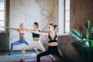 trois femmes pratiquent le yoga posture du guerrier 2