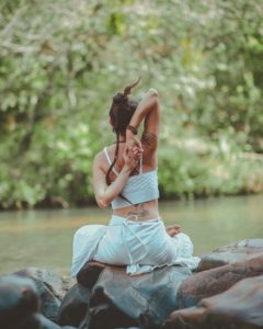 femme de dos en posture de gomuka asana au bord d'une rivière