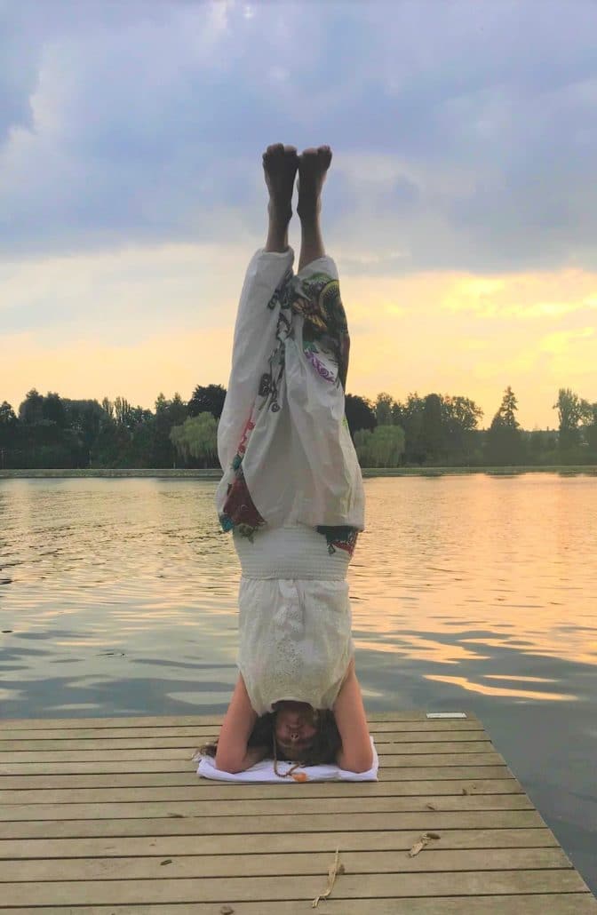 anne gauby professeur de yoga en posture sur la tête au bord d'un lac